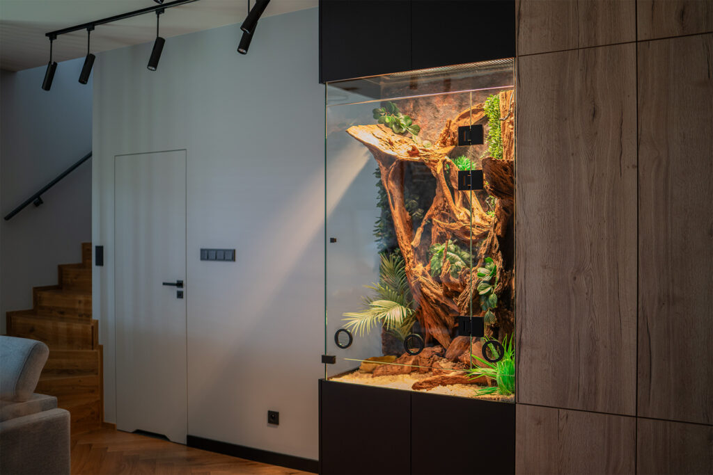 Eleganckie szklane duże terrarium dla węża w zabudowie meblowej.